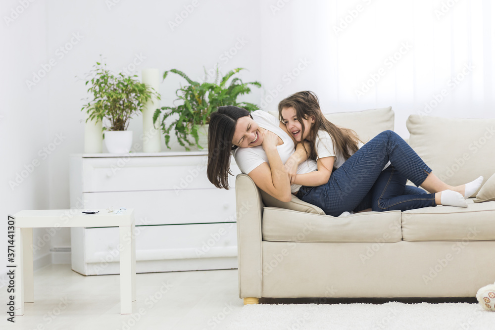 Fototapeta premium Photo of little girl playing with her mother on white sofa.