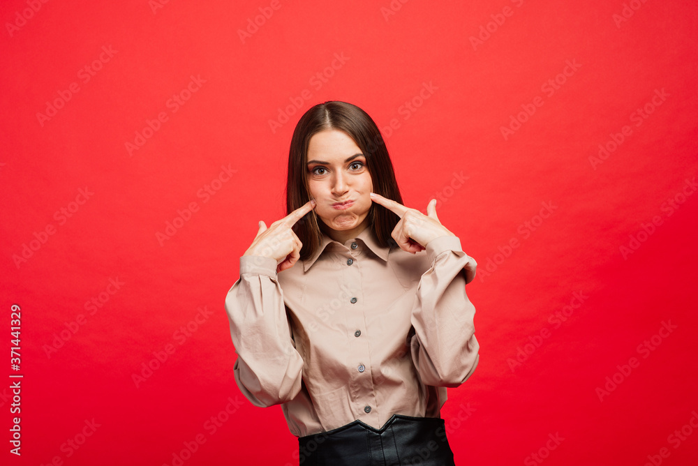 Fototapeta premium What is it. The female portrait isolated on red studio backgroud. The young emotional angry, scared woman looking at camera.The human emotions, facial expression concept.