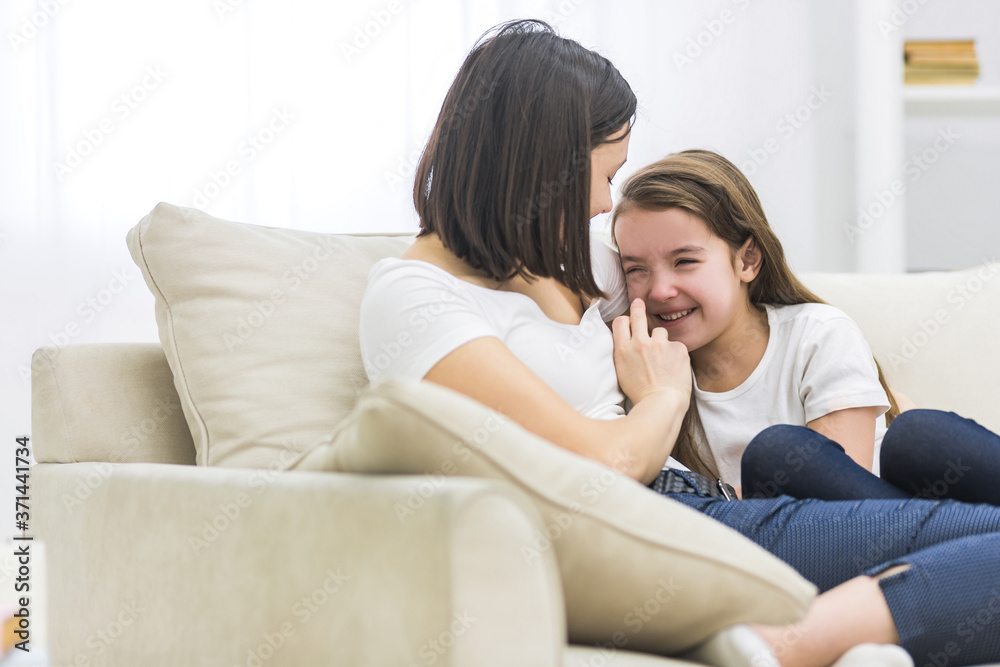 Photo of happy mother and daughter talking on sofa in living room.