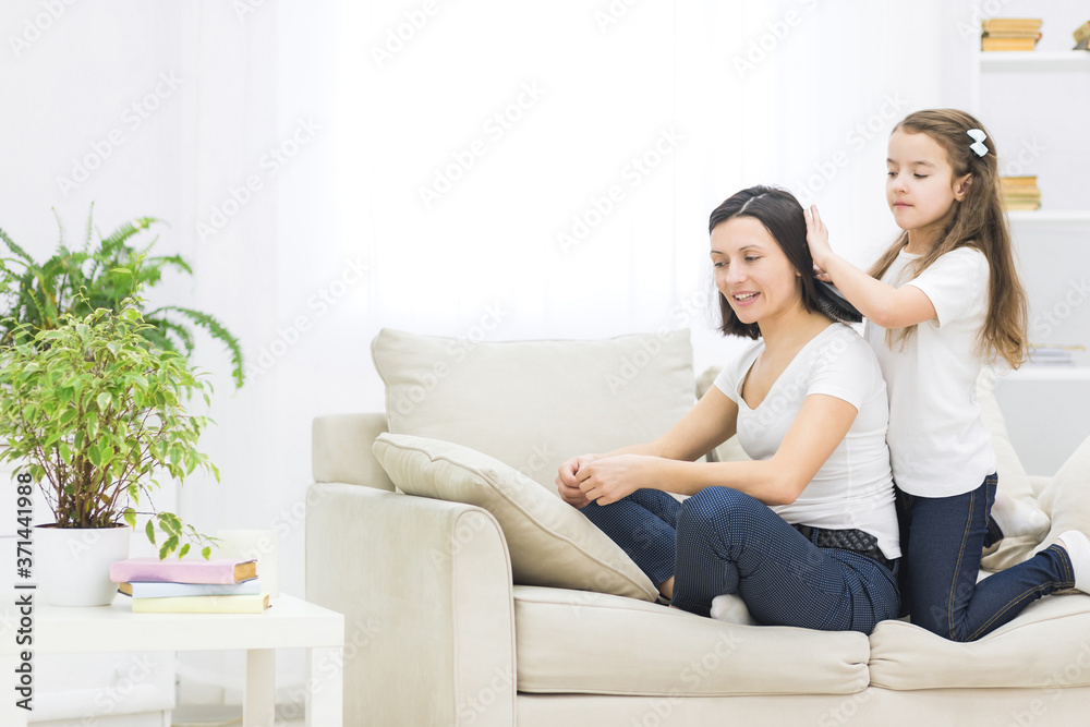 Photo of smiling mom with short dark hair and her beautiful little daughter who is brushing her hair.