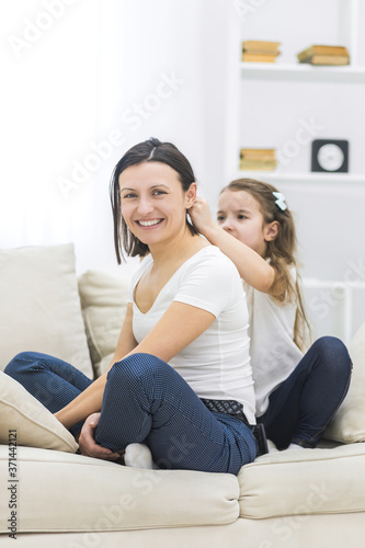 Happy smiling mother and daughter sitting on sofa.