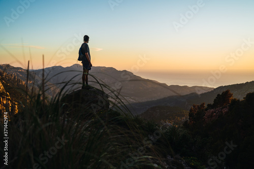 A man stands on a rock looking to the right while trekking during golden light on a mountain looking at the stunning views of Serra de Tramuntana (Mallorca, Spain)