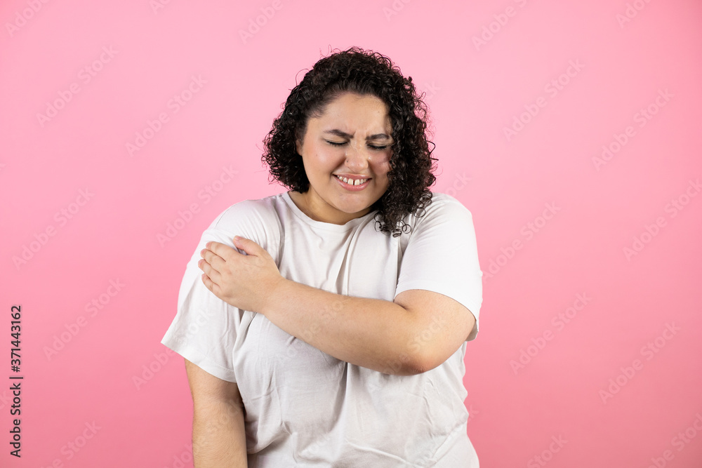 beautiful woman with pain on her shoulder and a painful expression on pink background. beautiful woman with pain on her shoulder and a painful expression on pink background.