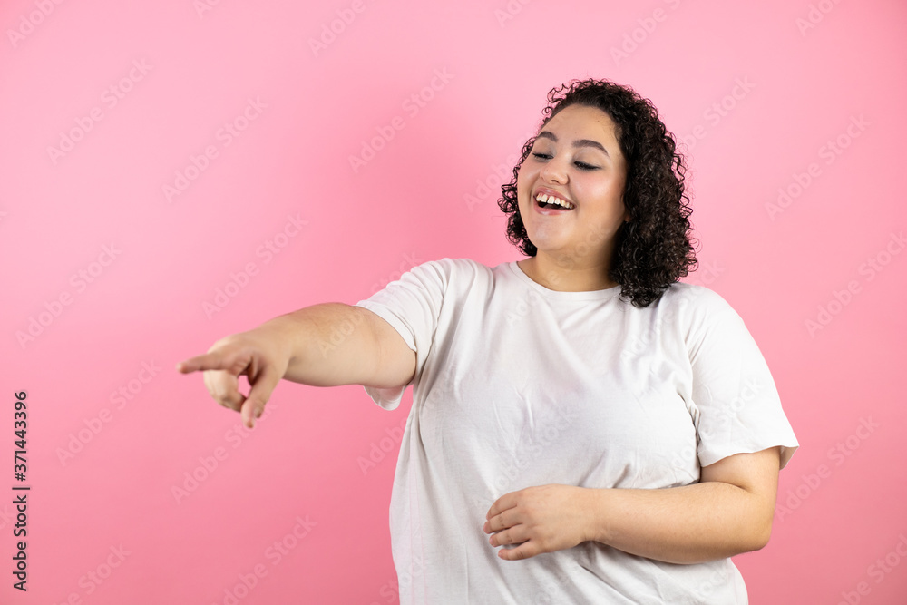 Young beautiful woman over pink background laughing at you, pointing finger to the camera with hand over body, shame expression Young beautiful woman over pink background laughing at you, pointing finger to the camera with hand over body, shame expression