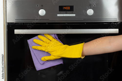 Woman's hand in yellow glove cleaning door of an oven