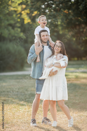 Young beautiful family walks in the park. Family portrait in the sunset light. Summer picnic.