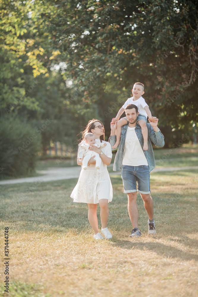 Naklejka premium Young beautiful family walks in the park. Family portrait in the sunset light. Summer picnic.