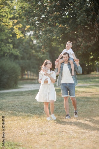 Young beautiful family walks in the park. Family portrait in the sunset light. Summer picnic.