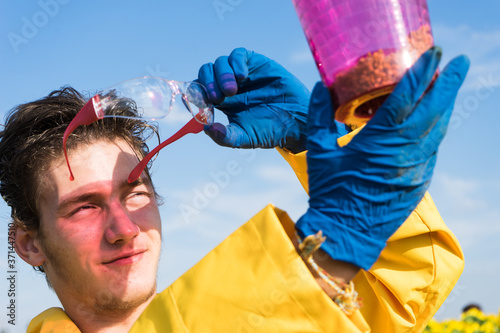 fashionable portrait of a young handsome man with glasses and a yellow raincoat in a sunflower field. A man collects fruit-bearing sunflower flowers in atransparent container. bright colors, art photo photo