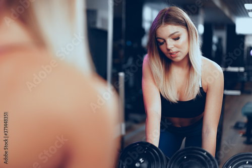 Curvy fit young blonde woman lifting dumbbell in a gym