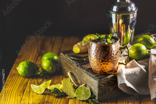 Moscow mule alcoholic cocktail in copper mug with crushed ice, mint and lemon over minton dark wooden table with amazing backlight, copy space. Close up view, copy space photo