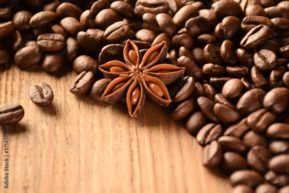 Anise and a lot of coffee beans lie on a wooden brown table. There is an empty space at the bottom left. Anise and a lot of coffee beans lie on a wooden brown table. There is an empty space at the bottom left.