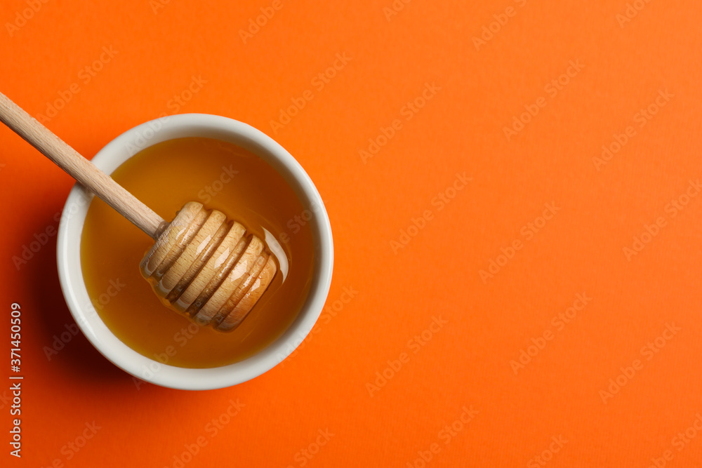 Bowl with honey and dipper on orange background, top view Bowl with honey and dipper on orange background, top view