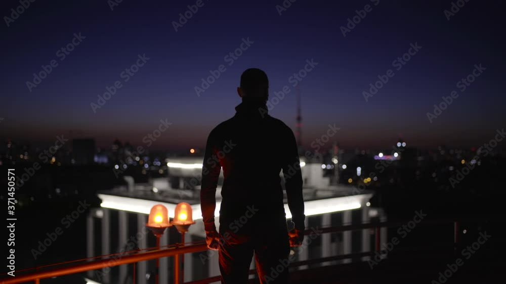 Decisive man looking at night city from roof, escaping in darkness, secret agent Decisive man looking at night city from roof, escaping in darkness, secret agent