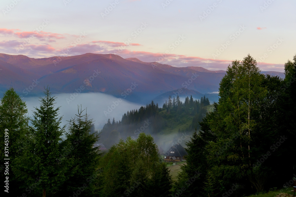 Dawn in the mountains. A country house in a meadow among the mountains, fog creeping in the valley.