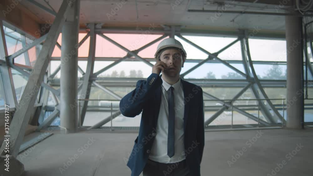 Young confident contractor in elegant suit on building site talking to partner on smartphone Young confident contractor in elegant suit on building site talking to partner on smartphone