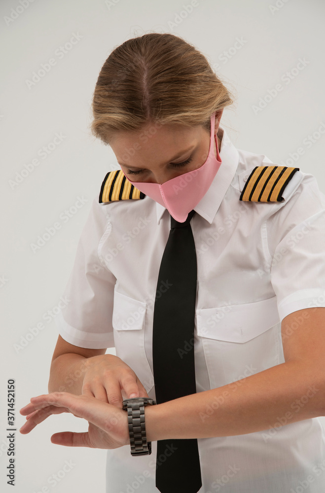 Wiltshire, England, UK. August 2020.  Airline pilot checking her wristwatch and wearing a face mask during the Covid-19 lockdown.