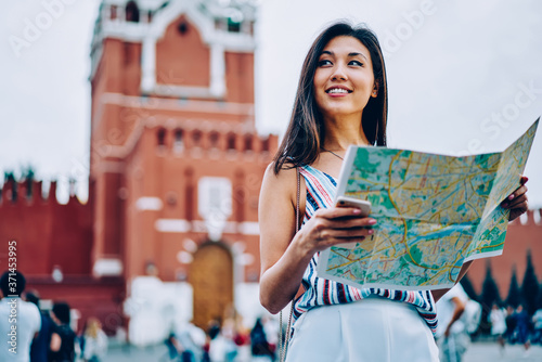 Attractive asian girl standing on red square in moscow enjoying sightseeing tour with map, cheerful female tourist getting to location near Kremlin on background planning next route in Moscow