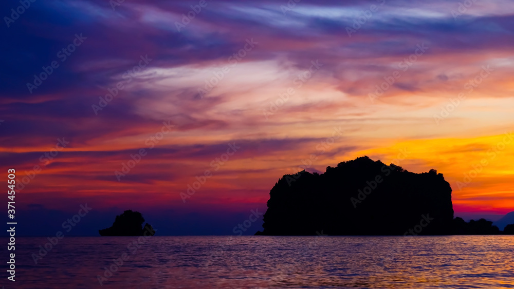 A beautiful setting sun behind the silhouette hills and rocks with its reflection over the sea waves at Tanjung Rhu Beach, Langkawi,