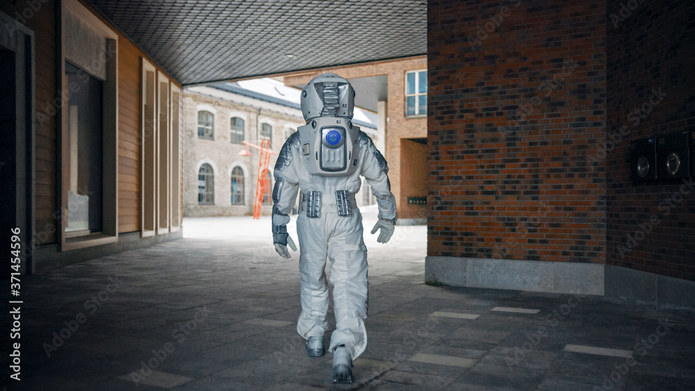 Low Angle Shot of a Confident Handsome Astronaut from the Back in a Neighbourhood with Modern Scandinavian Buildings. Man in Futuristic Suit with Technological Panel on His Hand.
