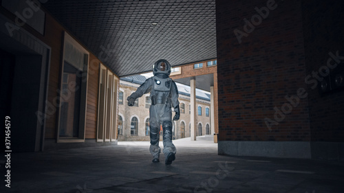 Low Angle Shot of a Confident Handsome Astronaut is Walking Towards the Camera in a Neighbourhood with Modern Scandinavian Buildings. Man in Futuristic Suit with Technological Panel on His Hand. © Gorodenkoff