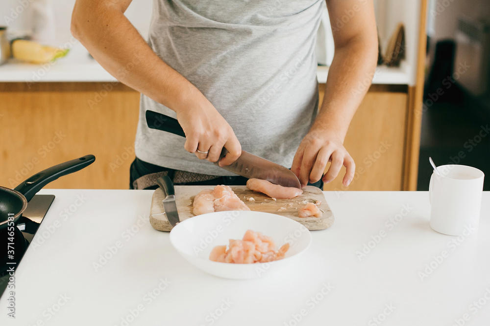 Person cutting chicken fillet with knife on wooden board on modern white kitchen. Process of making home pizza, hands close up. Home cooking concept Person cutting chicken fillet with knife on wooden board on modern white kitchen. Process of making home pizza, hands close up. Home cooking concept