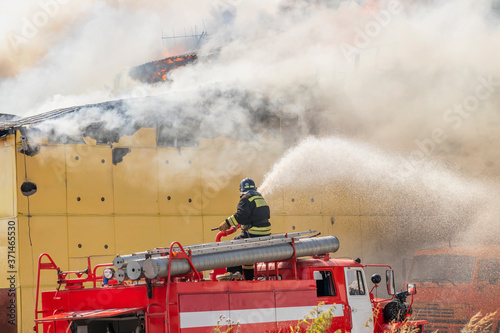 Fire extinguishing. Fire engine. A firefighter directs a stream of water at a burning building.