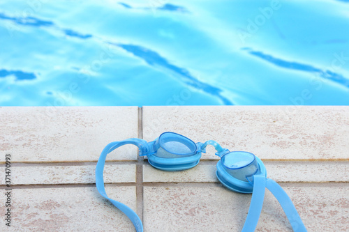 Blue swimming pool goggles on the edge of a private pool. Focus in foreground.