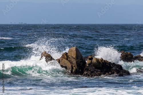 White ocean waves splash on craggy rocks on the shore of Monterey Bay at Pacific Grove, California.