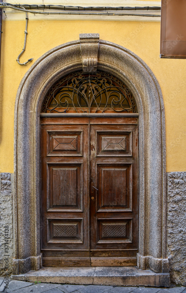 Close-up of an old wooden door with arched stone frame on a yellow wall, Italy
