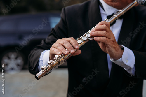 A musician at the event in a frock coat and bow tie plays the flute. Сlose-up of hands and tools