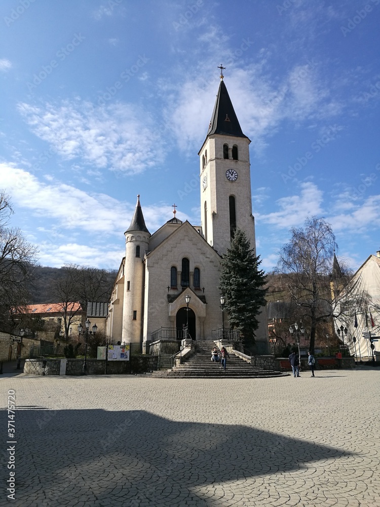 A church with a clock tower in front of a building in Tokaj
