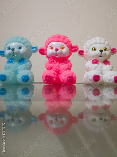 Sheep dolls of different colors placed together showing their reflections on the glass.