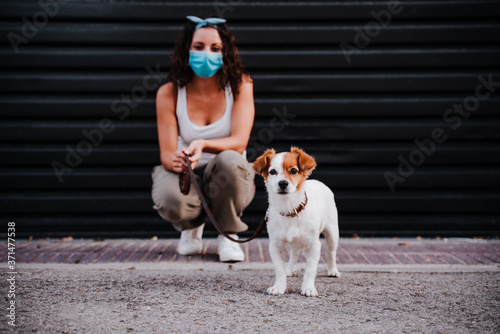 Fototapeta Naklejka Na Ścianę i Meble -  young woman outdoors wearing protective mask, cute jack russell dog besides. New normal concept
