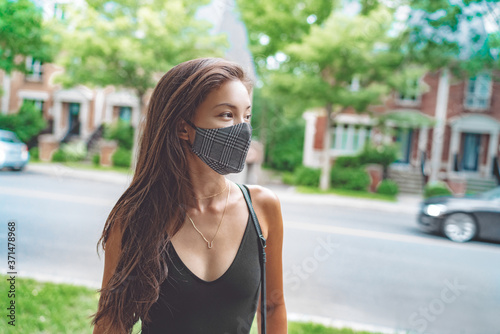 Asian woman walking in city street wearing face mask for COVID 19 prevention. Happy young student with fashion pattern cloth mouth covering outside. Corona virus concept.