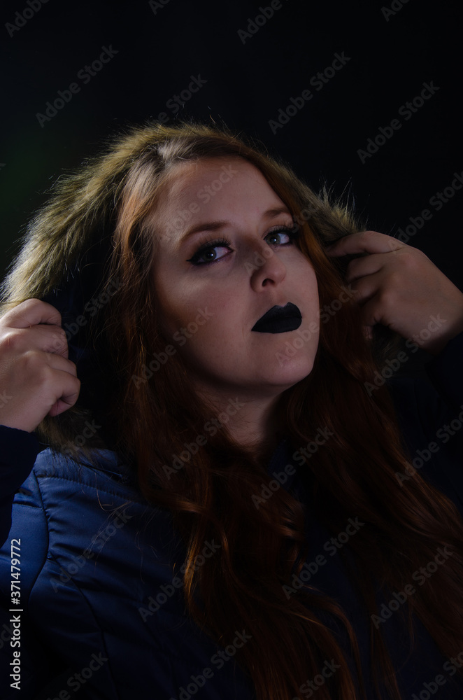 Portrait of a redhead with coat made in studio, low key image, with black background. Portrait of a redhead with coat made in studio, low key image, with black background.