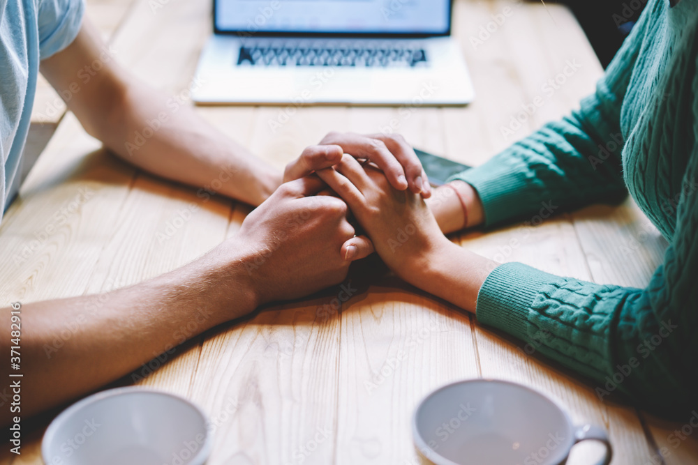 Fototapeta premium Cropped image of man and woman in love steady holding each other hands.Concept of sincere and trust relationship between young male and female sitting at wooden table in comfortable place
