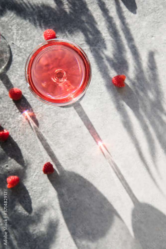 Smash gin alcoholic cocktail. Long raspberry drink on gray stone background, copy space. Sunlight through a glass of bevarage. Sun hard light shadow reflection Smash gin alcoholic cocktail. Long raspberry drink on gray stone background, copy space. Sunlight through a glass of bevarage. Sun hard light shadow reflection