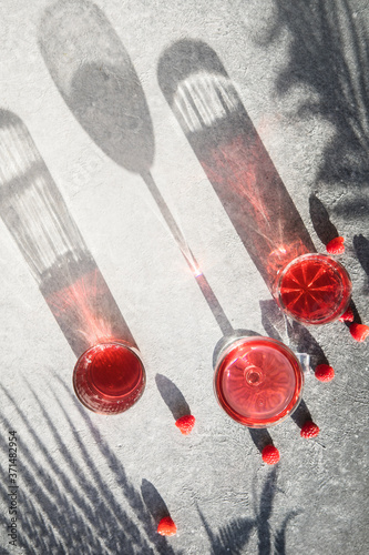 Smash gin alcoholic cocktail. Long raspberry drink on  gray stone background, copy space. Sunlight through a glass of bevarage. Sun hard light shadow reflection photo