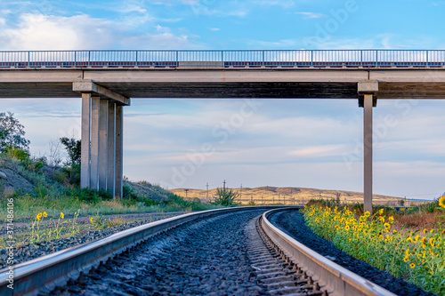 Railway tracks passing under a road bridge against a blue sky