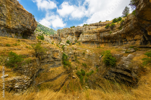 Baatara gorge waterfall in Lebanon. Unusual rocky landscape. Balaa Sinkhole caves and formations covered with green plants and dry grass.