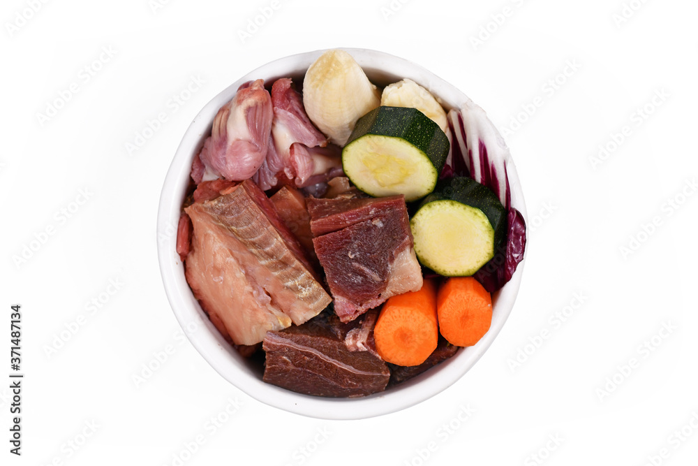 Dog bowl with species appropriated raw food like chunks of raw meat, fish, chicken stomache and vegetabls like carrots and zucchini isolated on white background