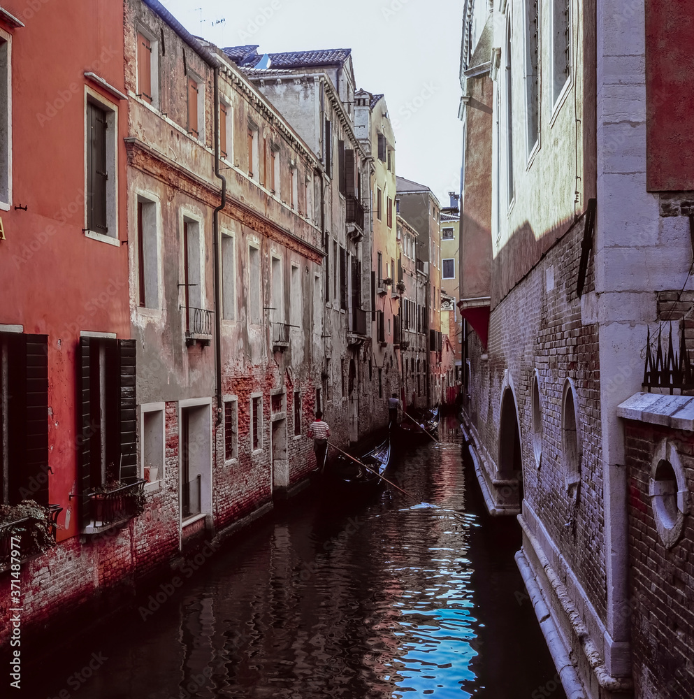 Two gondolas navigating a  narrow water channel in Venice, shot with analogue slide film technique