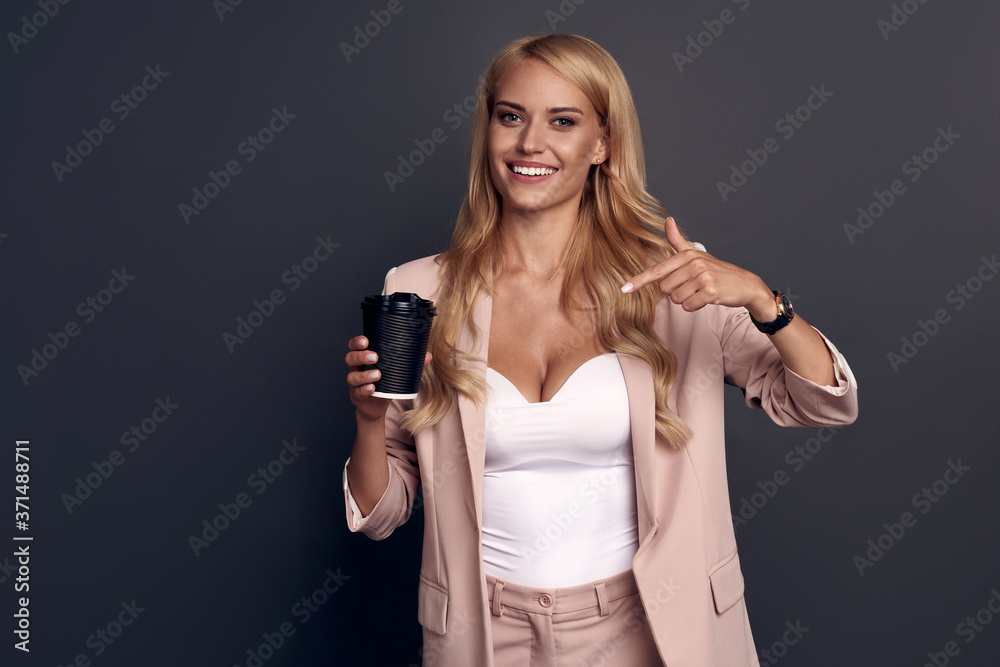 Image of smiling businesslike woman in pink suit looking at camera with takeaway coffee in hand isolated over gray background Image of smiling businesslike woman in pink suit looking at camera with takeaway coffee in hand isolated over gray background