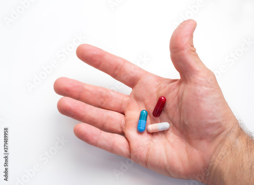 hand holding red, blue and pink- white pills over a white background