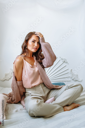 Model girl in a stretched knitted jacket on the bed. Demonstration of clothing