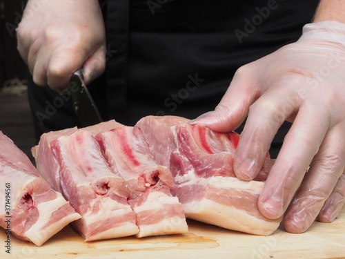 Fototapeta Naklejka Na Ścianę i Meble -  a chef in gloves and a black apron cuts a pork loin into steaks. the cooking of the steaks. meat. pork.