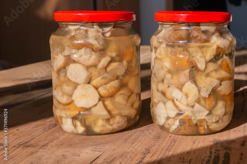 Canned mushrooms boletus in glass jars on wooden table