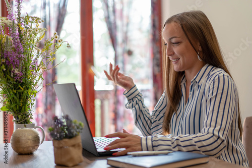 Portrait of successful young woman working remotely at laptop device. Smiling female copywriter enjoying free working schedule.