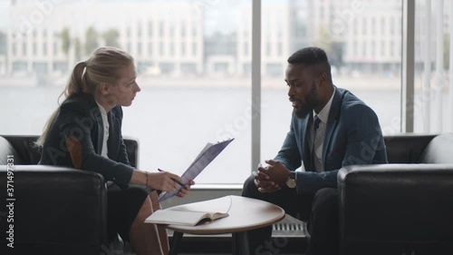 Young HR woman interviews afro-american male candidate for job sitting on couch in conference room